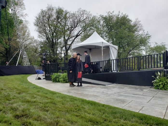 A graduate receiving a kiss at an outdoor graduation ceremony.