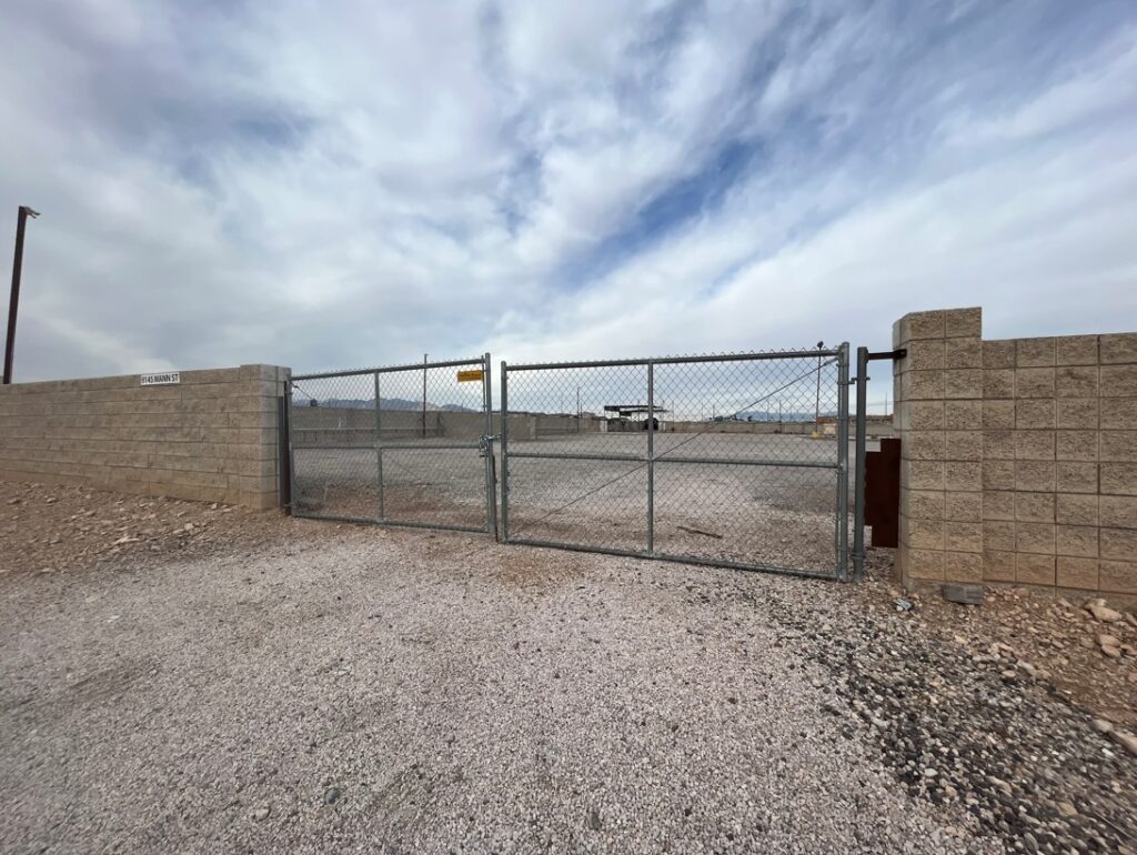 Chain-link gate between tan block walls at an empty lot.