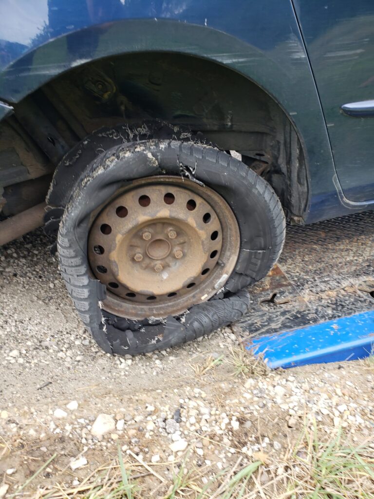 A severely blown-out and shredded car tire on a rusty rim.