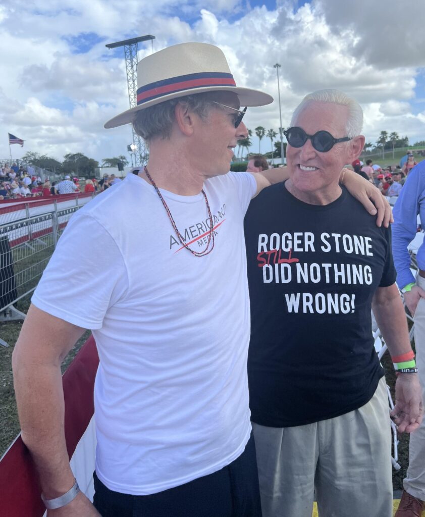 Roger Stone and a man at an outdoor political rally.